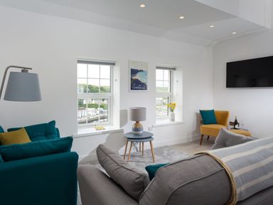 A sitting room with sofas chairs a lamp a side table and a wall mounted tv at Chy Lowen in Porthleven