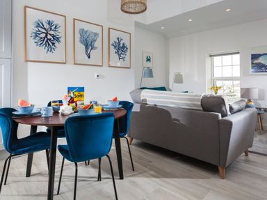 A dining table set with bowls and watermelon slices next to a grey sofa in a living room at Chy Lowen in Porthleven