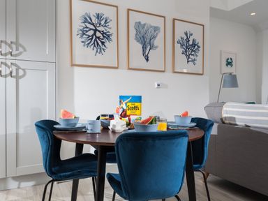 A dining area with a round table set with bowls of watermelon and orange juice surrounded by blue chairs at Chy Lowen in Porthleven