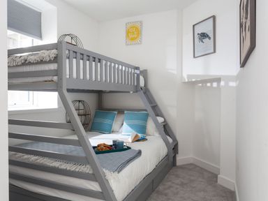 A small bedroom with a gray bunk bed blue pillows and a window at Chy Lowen in Porthleven