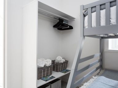 A bunk bed next to an open closet with hangers and baskets with rolled towels at Chy Lowen in Porthleven