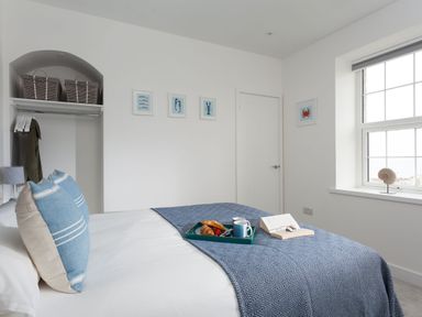 A bedroom with a bed pillows a window and a tray with food on the bed at Chy Lowen in Porthleven