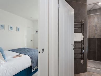 A bedroom with a bed and framed pictures on the wall next to a bathroom with a shower and towel rack at Chy Lowen in Porthleven
