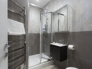 A bathroom with a glass shower enclosure a towel rack with white towels a wall-mounted sink and a toilet paper holder at Chy Lowen in Porthleven