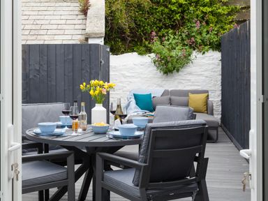 An outdoor patio area with a round table set with blue bowls and wine glasses and a sofa with colored cushions at Chy Lowen in Porthleven