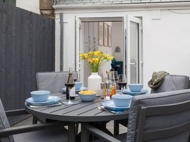 An outdoor dining table set with blue plates bowls glasses and a vase with yellow flowers at Chy Lowen in Porthleven