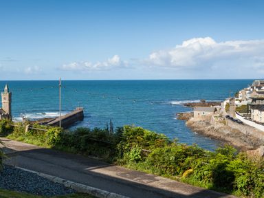 A coastal view with a stone pier, buildings on rocky shore, and the ocean under a blue sky at Chy Lowen Porthleven
