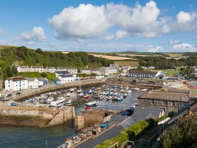 A harbor with boats docked along a stone pier next to houses and green hills at Chy Lowen in Porthleven