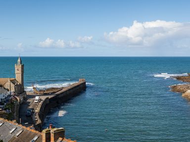 A coastal view with a stone clock tower and a pier extending into the sea at Chy Lowen in Porthleven