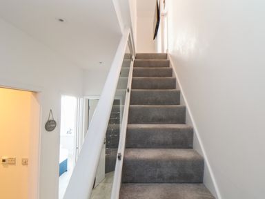 A carpeted staircase with glass side panels leading up in a white wall hallway at Chy Lowen in Porthleven