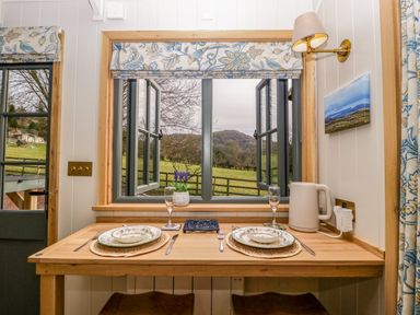 A dining table set for two with plates forks knives glasses and a kettle by a window with a view of fields at Evendine Hut at Evendine Cottage in Colwall Herefordshire