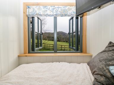 A bedroom with a bed near an open window showing a countryside view at Evendine Hut @ Evendine Cottage in Colwall Herefordshire