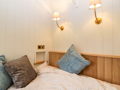 A bed with blue and brown pillows against a wood paneled wall with two wall lamps at Evendine Hut @ Evendine Cottage Colwall Herefordshire