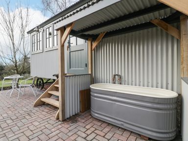 An outdoor covered area with a bathtub and steps leading to a raised door beside a small table and chairs Evendine Hut @ Evendine Cottage Colwall Herefordshire