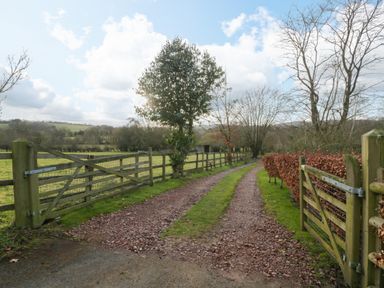 A gravel driveway with wooden gates and fences alongside trees and fields at Evendine Hut @ Evendine Cottage in Colwall Herefordshire