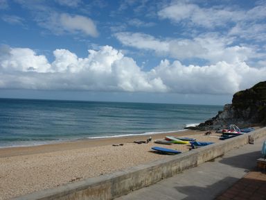 A beach with boats on the sand and a seawall under a partly cloudy sky at 2 Bayview in Torcross