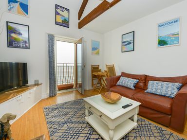 A living room with a leather sofa pillows coffee table and balcony door showing ocean view at 2 Bayview in Torcross