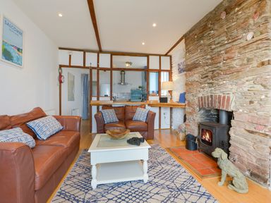 A living room with brown leather sofas a white coffee table a stone fireplace with a wood stove and a blue patterned rug at 2 Bayview in Torcross