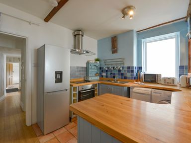 A kitchen with wooden counters a refrigerator oven microwave and window at 2 Bayview in Torcross
