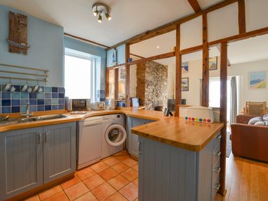 A kitchen with blue cabinets wooden countertops and a washing machine next to an open living area at 2 Bayview in Torcross