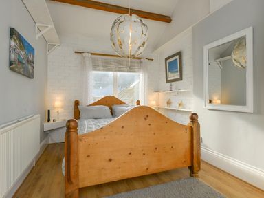 A bedroom with a wooden bed frame a window with curtains bedside shelves with lamps and decorations at 2 Bayview in Torcross