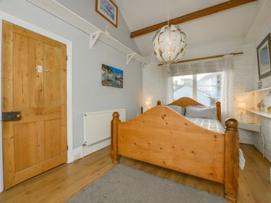 A bedroom with a wooden bed wooden door and large window at 2 Bayview in Torcross