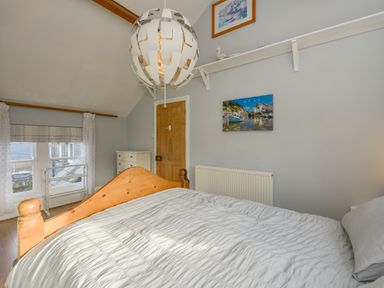 A bedroom with a wooden bed frame white bedding a wooden door white chest of drawers and a round pendant light at 2 Bayview in Torcross