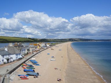 A pebble beach with boats on the shore and houses along a paved road by the sea at 2 Bayview in Torcross