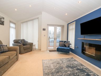 A living room with armchairs a wall-mounted television and a fireplace at Y Caban in Brynsiencyn