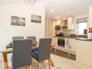 A kitchen and dining area with a glass table and gray chairs at Y Caban in Brynsiencyn