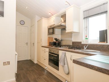 A kitchen with cream cabinets a gas stove oven microwave sink and window at Y Caban in Brynsiencyn