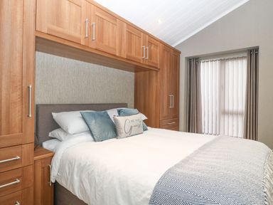 A bedroom with a double bed built into wooden cupboards and a window with vertical blinds at Y Caban in Brynsiencyn