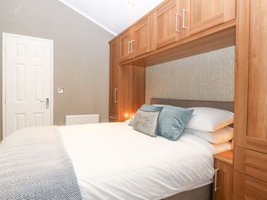 A bedroom with a double bed white bedding pillows and wooden overhead cabinets at Y Caban in Brynsiencyn