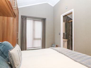A bedroom with a bed with pillows and blanket next to a window with curtains and an open door to a bathroom at Y Caban in Brynsiencyn