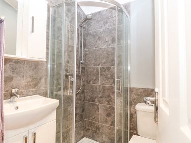 A bathroom with a corner shower enclosure a sink with cabinet and a toilet at Y Caban in Brynsiencyn