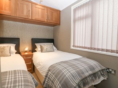 A bedroom with two single beds a nightstand and overhead cabinets at Y Caban in Brynsiencyn
