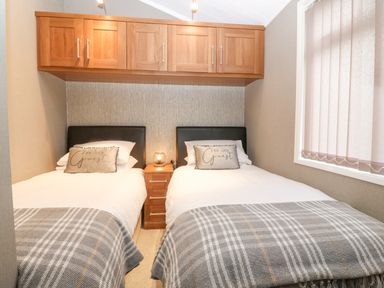 A bedroom with two single beds gray plaid blankets and wooden cabinets above the beds at Y Caban in Brynsiencyn