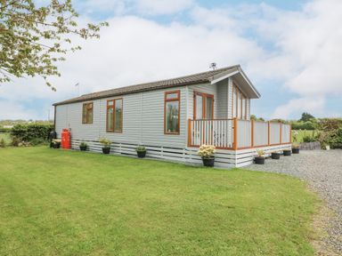 A single storey house with a small porch and potted plants on a lawn at Y Caban in Brynsiencyn