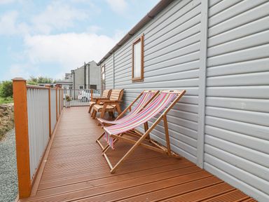 An outdoor wooden deck with two striped deck chairs and two wooden armchairs at Y Caban in Brynsiencyn