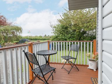 A small wooden deck with a black metal table and two chairs and a plant in a pot at Y Caban in Brynsiencyn