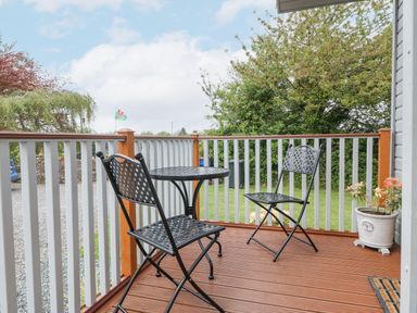 A small outdoor deck with two black metal chairs a matching round table and a potted plant at Y Caban in Brynsiencyn