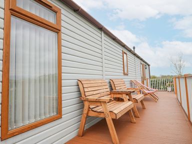 A deck with wooden benches and deck chairs attached to a building at Y Caban in Brynsiencyn