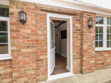 An open white door in a brick wall flanked by two black wall lamps at The Five Bells Inn in Upwell