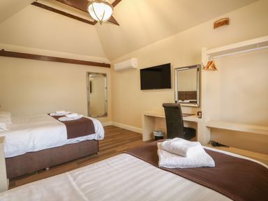 A hotel room with two beds a wall-mounted television a desk with a chair two mirrors and an open closet at The Five Bells Inn in Upwell