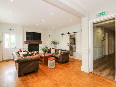 A seating area with brown leather sofas coffee table and a television above a fireplace at The Five Bells Inn in Upwell