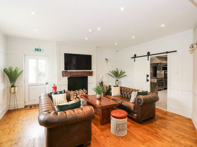 A sitting area with two leather sofas a wooden table plants a television above a fireplace and a sliding door leading to a kitchen at The Five Bells Inn in Upwell