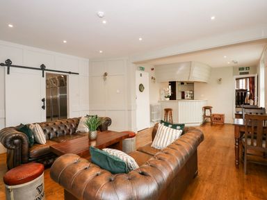 A seating area with leather sofas, wooden tables, and stools in a room with white walls and wood flooring at The Five Bells Inn in Upwell