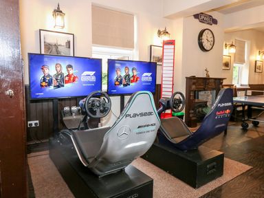 A room with two racing simulator seats and steering wheels in front of two screens showing f1 2021 at The Five Bells Inn in Upwell