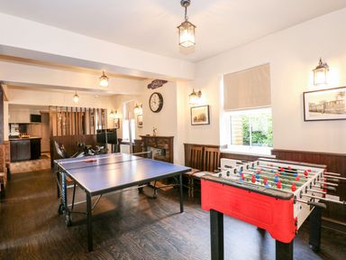 A game room with a table tennis table and foosball table with chairs and wall clock at The Five Bells Inn in Upwell