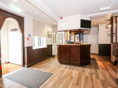 An entrance area with a wooden bar counter a window with a blind a coat rack and framed pictures at The Five Bells Inn in Upwell